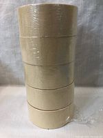 Five rolls of beige masking tape, 2 inches wide, shrink-wrapped in a stack against a fabric backdrop.