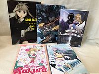 Set of five manga books arranged standing and lying flat featuring Soul Eater, Solo Leveling, School for Good and Evil, Cardcaptor Sakura, and Re:Zero titles.