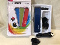 Photo of the Nova Professional Trimmer NS-216 in blue with comb attachments and USB charging cable inside plastic packaging. Box visible behind with colorful trimmer images and model info.