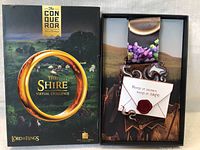 Image of the box packaging of The Shire Virtual Challenge Collectors Lanyard showing the lanyard and custom envelope charm inside the box.