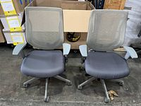 Front view of two AllSeating Zip mesh back task chairs side by side showing mesh backs, grey cushioned seats, and armrests with wear.