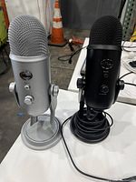 Pair of Blue Yeti USB microphones, one silver and one black, side by side on a table.