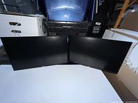 Both Dell monitors side by side, powered off, on a white surface with storage bins and boxes visible in background.