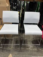 Pair of white high top bar height chairs with chrome frames, showing front view of seats and backs