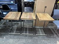 Three side tables lined up front view showing wood tops and metal C-shaped bases