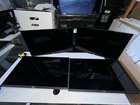 Four Dell 24-inch monitors positioned on a table without bases, screen facing up, all turned off.