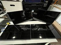 Four Dell flat panel monitors laid out on a white table with black glossy screens off, arranged two in front and two in back, showing the front face of the monitors.