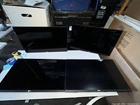 Four Dell 24-inch monitors placed side by side on a white table. Screens face upward, black bezels visible. No stands shown.