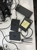 Six docking stations including four Dell branded docking stations, two silver USB-C multiport adapters, and attached cables.