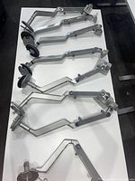 Eight silver Humanscale monitor arms laid flat on a white surface showing the articulated arms and desk mounting clamps.