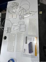 Overview of 3 Apple wireless keyboards, 5 Apple Magic Mice, a white USB hub, white Apple power adapters, charging cables, and a boxed Netgear 8-port Ethernet switch.