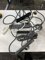 Five extension cords including power strips with multiple outlets and On/Off switches piled on a white table.