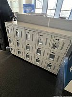 Metal locker bank with 12 individual doors, showing the entire unit and its placement in an office space.
