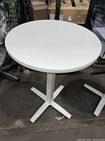 Front angle view of white round height bar table with metal base showing minor scratches on the tabletop surface.