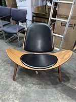 Front angled view of the Hans Wegner style shell lounge chair showing wooden frame and black cushions.