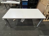 Photo of a rectangular white work table with silver metal legs viewed from above at an angle.