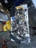 Photo of table with multiple tangled cables including power cables, HDMI, ethernet cables, two black keyboards, and three remote controls.
