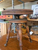 Side view showing the wooden turned legs and claw metal feet, as well as the adjustable screw mechanism beneath the seat.