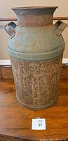Full side view of the large antique metal milk can showing the overall shape, shape of the handles, and the rustic patina.