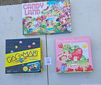 Top view showing boxes of Candy Land, Pac-Man, and Strawberry Land board games on a white table.