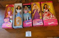 Five collectible Barbies in their original boxes displayed side by side: Make It Awesome Barbie, Dorothy Barbie (Wizard of Oz), Tooth Fairy Barbie, Graduation Barbie, and Evening Flame Barbie.
