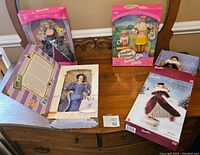 Four Barbie dolls in original boxes, displayed upright on wooden surface. Various thematic packaging.