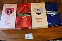 Four Barbie dolls in original boxes displayed on a wooden surface, showing front of boxes with labels and designs.
