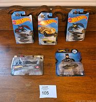 Overview photo showing all five Batman themed Hot Wheels cars in original packaging arranged on a wooden surface.