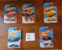Five Hot Wheels cars in original packaging laid out on wood surface, showing all card fronts and car details.