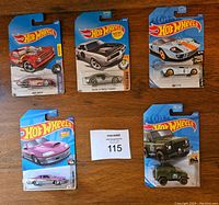 Five Hot Wheels cars in original packaging placed on a wooden table. Various models visible with blue packaging and Hot Wheels logo.