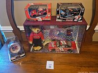 Overall view of NASCAR collectibles including two boxed remote control cars, a clock, and a display case with NASCAR car and plush bear