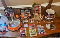 Overview of the lot showing multiple NASCAR collectibles including diecast cars, a dog bowl, mugs, and small collectible cards tidily displayed on a wood surface.