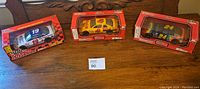 Three NASCAR diecast cars, 1:24 scale, in original boxes placed on wooden surface.