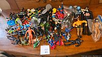 Photo showing an assortment of superhero figures including Marvel and DC characters, loose on wooden table, with some figures bagged.
