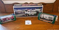 Overview photo of the three Hess trucks on a wooden surface, showing original boxes including a large box for Toy Truck and Space Cruiser and smaller green display boxes for the fuel tanker and fire truck.