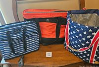 Three insulated bag coolers on a wooden table, showing the striped SCOUT cooler, orange cooler, and star-patterned cooler.