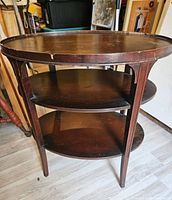 Front-side view of the three tiered wooden side table showing the legs, shelves, and oval tabletop with some wear and chips.