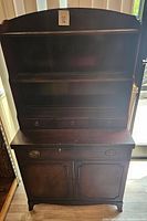 Front view of the dark wooden bookshelf hutch with three shelves, three small drawers, and a cabinet base.