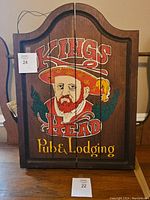 Front view of closed wooden dart board cabinet with painted Kings Head Pub & Lodging logo of a man with a red hat and beard.