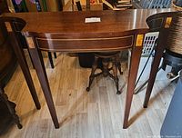 Front view of vintage serpentine console table showing the curved front apron, tapered legs, and inlaid rectangular wood details.