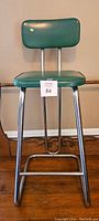 Full view of green vinyl mid-century modern stool with chrome tubular metal legs and backrest supports.