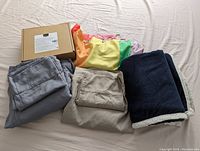 All items displayed together showing sheets, sherpa blanket, boxed taupe sheet set, and folded rainbow shower curtain