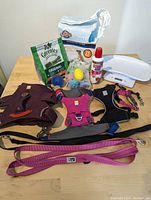 Overview of assorted dog supplies showing puppy pads, Greenies treats, various toys, pet scale, harnesses, and leashes