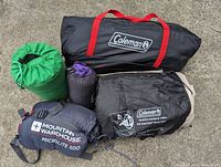Camping sleep supplies including tents, sleeping mats, mattress, sleeping bag, and pillow packed in storage bags on concrete surface.
