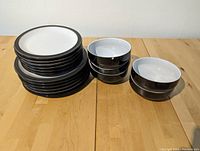 Stack of multiple large and small plates on left and groups of bowls on right on a wooden table.