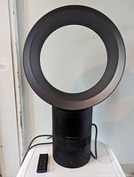 Front view of Dyson AM06 fan with loop amplifier, base, and remote on table