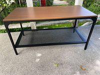 Ikea FJALLBO coffee table angled side view with brown solid wood top and black metal frame with mesh shelf below