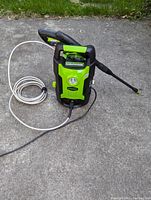 Front view of the green and black Greenworks pressure washer unit with white hose and black spray wand attached and laid to side.