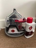 Front and side views of Hoover ClearSlate carpet spot cleaner and bottle of carpet cleaning formula on beige carpet.