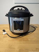 Front view of the Instant Pot with digital display panel and attached power cord, placed on a wooden surface.